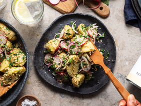 a photo of potato salad on a black plate with a wooden fork poking into it